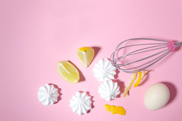 Top view of delicious meringues, pieces of lime, egg and whisk on the pink background