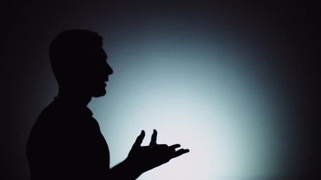 Silhouette of a man. The shadow of a man on a light background. A man. listens to the interlocutor, responds to him, actively gesticulates. Emotions, conversation, gestures.