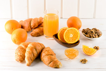breakfast of oranges and orange juice with fresh croissants on a white wooden table, place for design