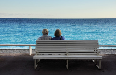 Naklejka na ściany i meble Old couple sitting on bench viewing the blue Mediterranean. Promenade des Angles, Nice, France.