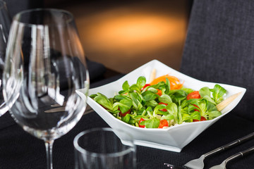 Fresh vegetable salad with basil in a white salad bowl on the table.