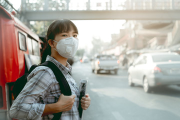 A student asian girl wearing PM 2.5 dust mask are in a city full of dust and smoke.