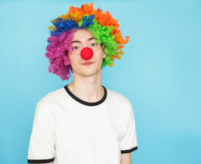 young funny male teenager in white t-shirt on blue background in clown wig