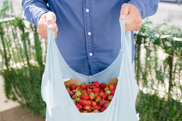 Person holding bag with healthy nutritious strawberries on groceries shopping market background,...