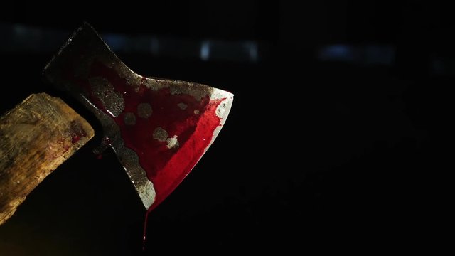 Axe with natural blood on the dark background. Close-up shot