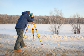 the surveyor takes measurements. the surveyor works in the winter on the nature. a man works with a...
