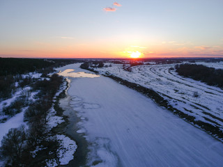 The forest and the frozen river with the appearance of thawed patches in the spring at sunset, when there is still snow in Russia from the height