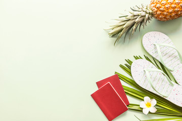 Travel flat lay items: two passports, fresh pineapple, beach slippers, tropical flower and palm leaf lying on green background. Place for text. Top view. Summer concept