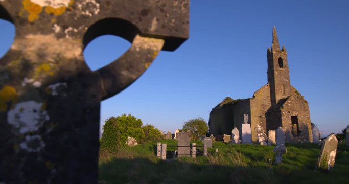 Slow pan across celtic cross graveyard cemetery to ruined church blue sky