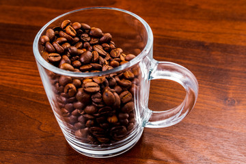 Roasted coffee beans in a glass cup isolated on a rustic dark wood table background