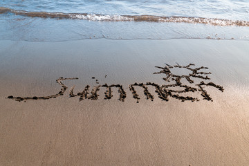 Summer handwritten on beach sand. Water sea background.