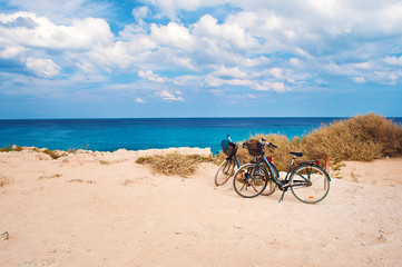 Two bicycles with baskets parked against deep blue azure water