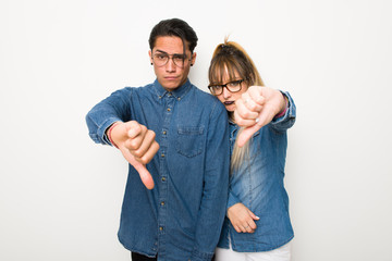 Young couple with glasses showing thumb down sign with negative expression