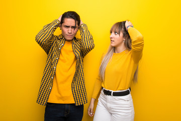 Young couple over vibrant yellow background takes hands on head because has migraine