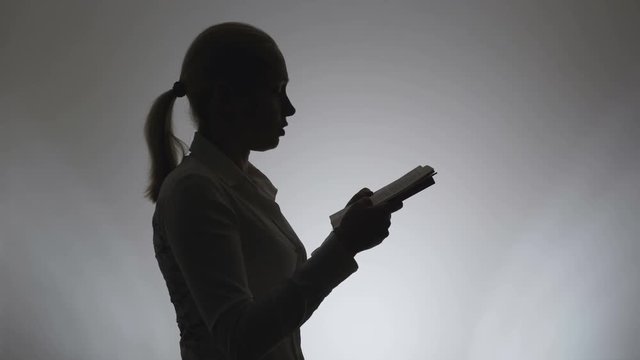 Silhouette of a woman with a book in her hands. Woman woman carefully reads a book.