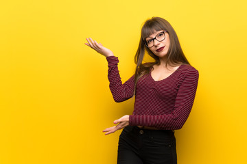 Woman with glasses over yellow wall extending hands to the side for inviting to come