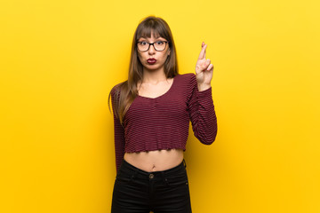Woman with glasses over yellow wall with fingers crossing and wishing the best