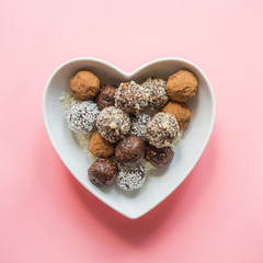 Homemade energy balls with cacao, nuts, and coconut flakes in plate as heart on pink. Concept healthy sweet food. Vegan dessert.