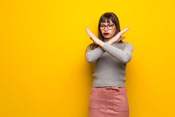 Woman with glasses over yellow wall making NO gesture