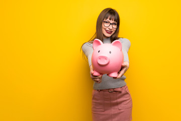 Fototapeta na wymiar Woman with glasses over yellow wall holding a piggybank