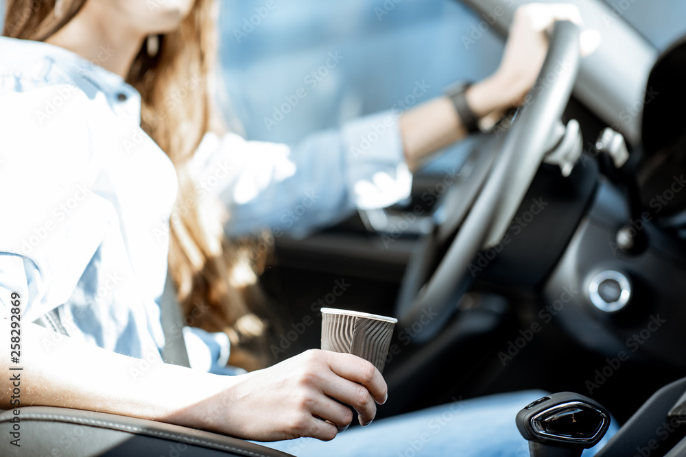 Wall mural Woman holding coffee cup while driving a car, close-up view focused on the cup