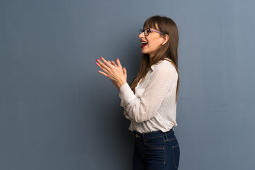 Woman with glasses over blue wall applauding after presentation in a conference
