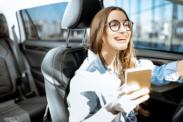 Young and cheerful woman using smart phone while driving a modern car in the city
