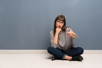 Woman with glasses sitting on the floor with thumbs up because something good has happened