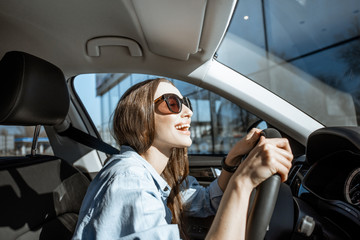 Young and cheerful woman enjoying while driving a modern car in the city, wide angle view
