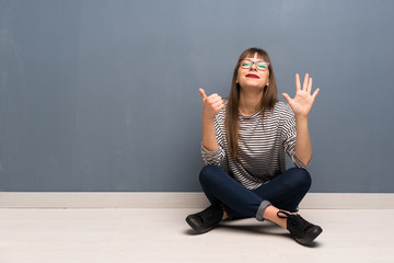 Woman with glasses sitting on the floor counting six with fingers