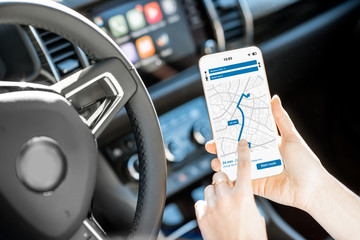 Close-up of a smartphone with navigation app in the modern car with monitor on the background