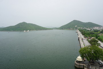 aerial view of the Hussain sagar lake at lakeside walkway in Udaipur, Rajasthan with view of rain soaked Aravali mountain range in the background