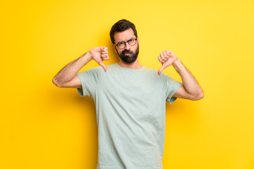 Man with beard and green shirt showing thumb down with both hands - obrazy, fototapety, plakaty