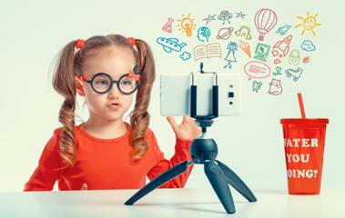 beautiful cute little blogger girl recording a video with smartphone and media icons flying