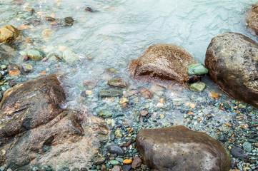 Boulders and pebbles on the bank of a river with milky green colour water