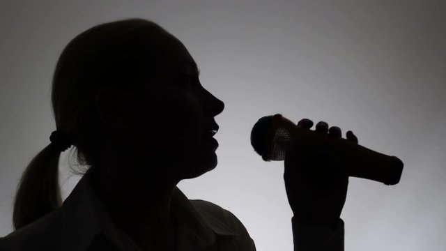 Silhouette of a woman on a white background. A woman sings emotionally into a microphone.