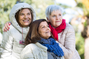 Fototapeta premium gruppo di trea amiche mature ridono felici con i piumini bianchi in un parco
