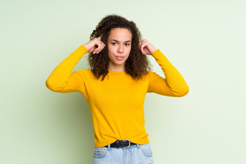 Dominican woman over isolated green background having doubts and thinking