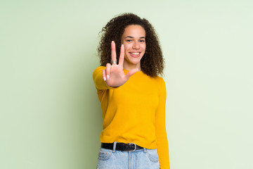 Dominican woman over isolated green background happy and counting three with fingers