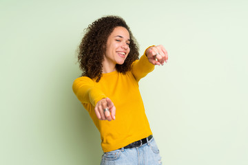 Dominican woman over isolated green background points finger at you while smiling