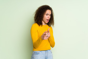 Dominican woman over isolated green background pointing to the front and smiling