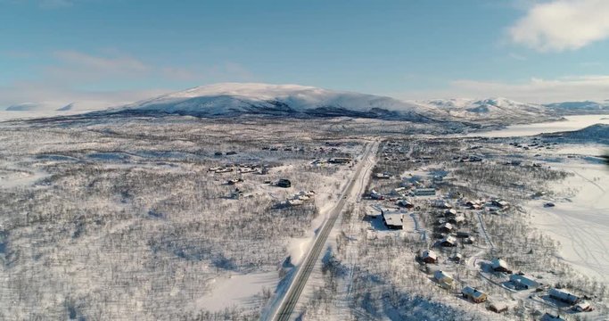 Kilpisjarvi village, C4k aerial, tilt, drone shot, towards a north scandinavian town, in snowy arctic circle wilderness, on a sunny, winter day, in Kilpisjrvi, Enontekio, Lapland, Finland