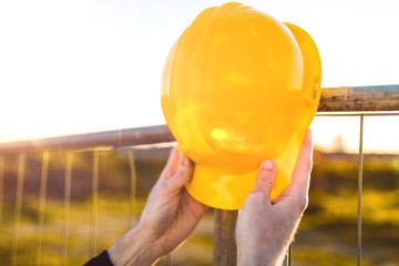 Inizio lavoro in cantiere. Mani di un operaio prendono il caschetto giallo di sicurezza in plastica...