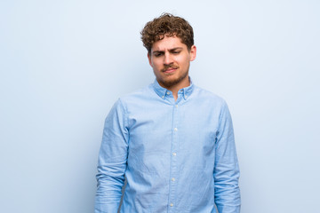Fototapeta premium Blonde man over blue wall with sad and depressed expression