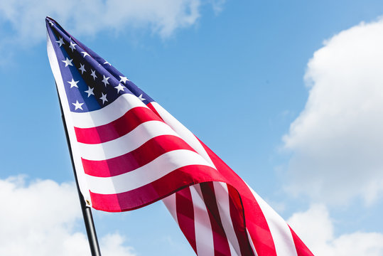 low angle view of stars and stripes on american flag against blue sky with clouds