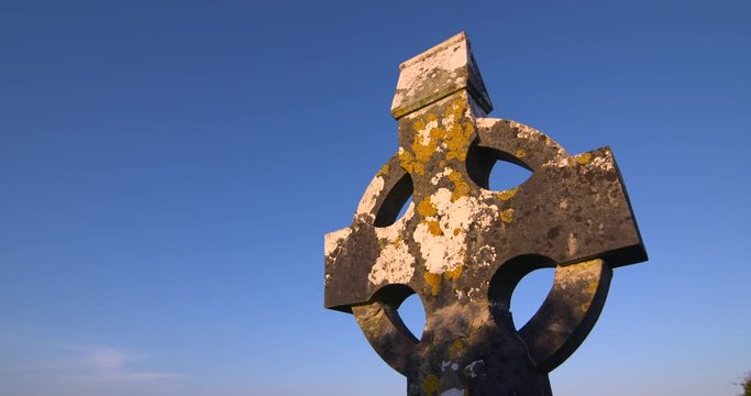 Ancient Irish celtic cross graveyard cemetery headstone golden sunshine blue sky