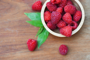Fresh raspberry in wooden bowl / Close up red raspberries fruit and green leaf top view