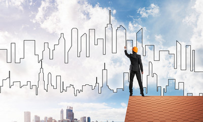 Man architect draw silhouette of modern city on blue sky. Mixed media