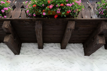 Part of the wooden balcony construction decorated with flowers against a white plaster wall.