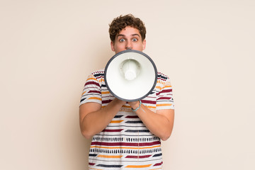 Blonde man over isolated wall shouting through a megaphone